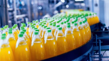 Plastic bottles of orange juice on a conveyor belt highlighting the need for accurate Declaration of Compliance documentation for food contact materials