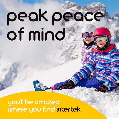 Two kids sitting on the snow in their winter sportwear with a mountain in the background